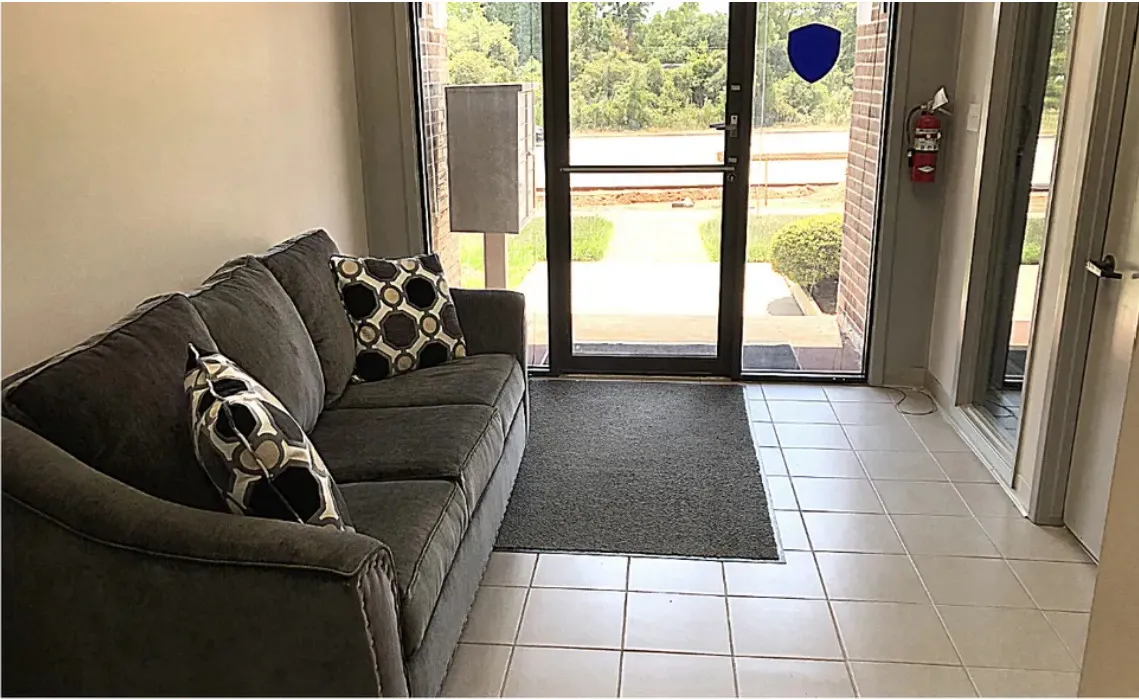Building A entrance lobby: tiled floor, a sofa, and full-height glass doors looking out to the parking lot.