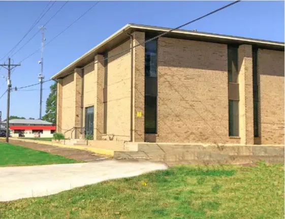 Building B viewed along the sidewalk from FM 2854, with lawn and mature trees on the approach.